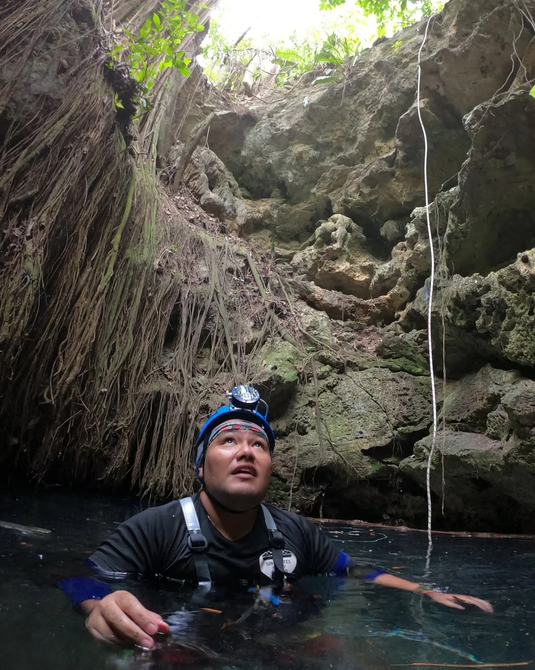 Exploración en el agua de un cenote, bajo una abertura entre rocas y raíces